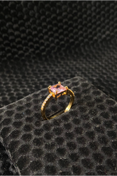 Gold ring with a pink gemstone on a black textured surface