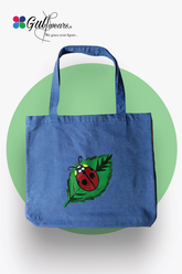 A blue painted tote bag with a green and red ladybug design on the front, displayed against a white background.