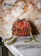 A vibrant pink potli bag with multicolored beadwork and tassel detailing, placed on a marble surface.
