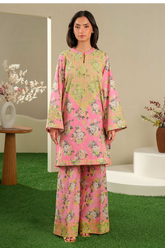 Woman wearing a pink floral outfit standing in a decorative indoor setting with plants and a table.