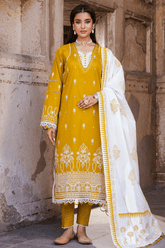 Woman wearing a mustard yellow and white embroidered traditional outfit against a stone wall.