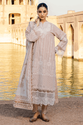 Woman in a traditional outfit standing by a water body with historical architecture in the background