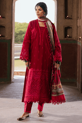 Woman in a red traditional outfit with a patterned scarf standing in a doorway.