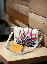 A white thread embroidered clutch bag with floral patterns, displayed on a wooden surface, with an orange business card holder in front.