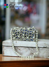 An off-white clutch bag with pearl accents and intricate Gotta work, placed on a wooden surface.