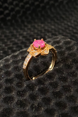 Gold ring with a pink gemstone on a black textured surface