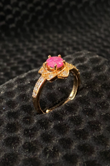 Gold ring with a pink gemstone on a black textured surface