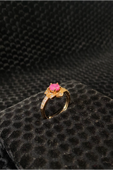 Gold ring with a pink gemstone on a black textured surface