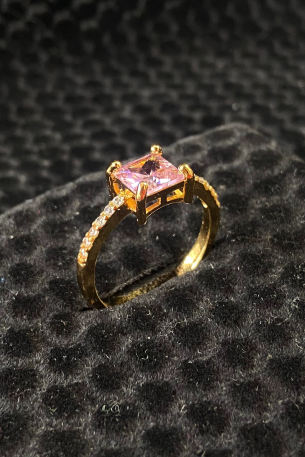 Gold ring with a pink gemstone on a black textured surface
