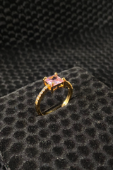 Gold ring with a pink gemstone on a black textured surface