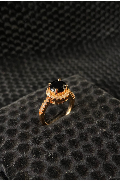 Gold ring with a black gemstone on a textured black surface