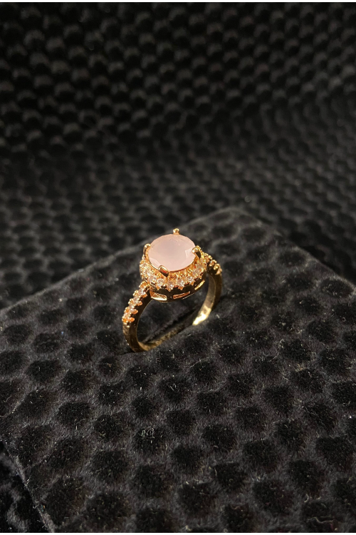 Gold ring with a pink gemstone on a black textured surface