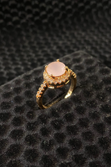 Gold ring with a pink gemstone on a black textured surface