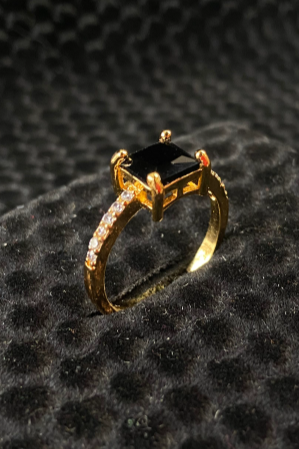 Gold ring with a black gemstone on a textured black surface