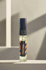 Small bottle of WARMAS perfume on a reflective silver surface with a gray background