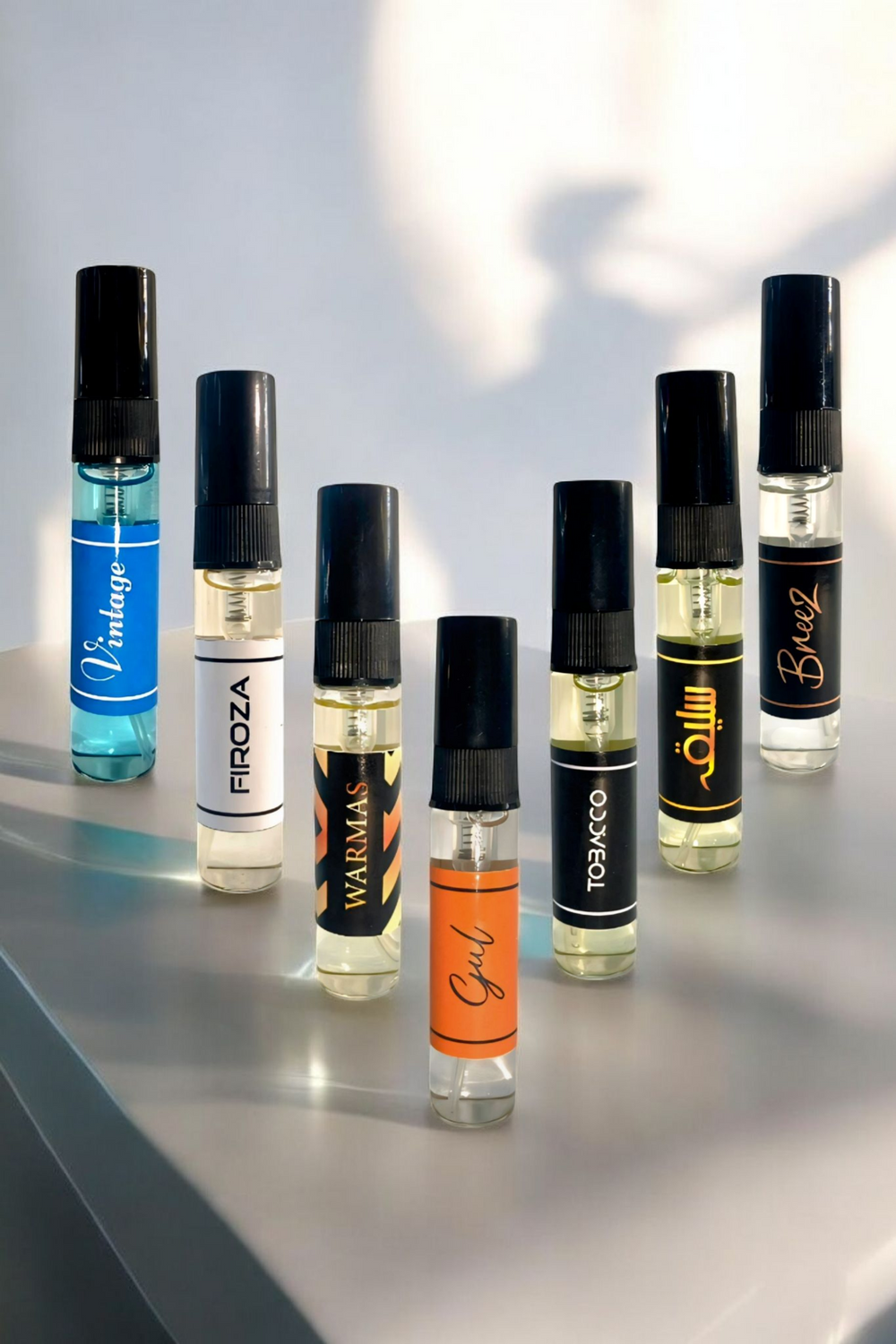 Row of small perfume bottles with black caps on a reflective surface.