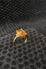 Gold ring with a large orange gemstone on a textured black surface