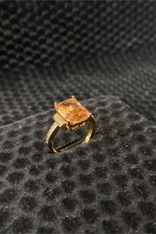 Gold ring with a large orange gemstone on a textured black surface