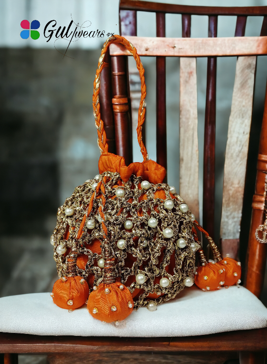 A bright orange potli bag with intricate copper gotta work, displayed on a wooden chair.