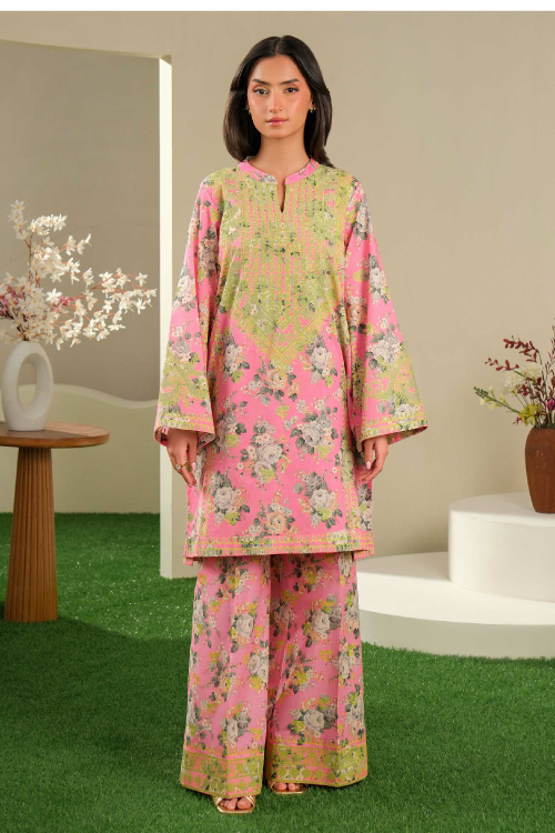 Woman wearing a pink floral outfit standing in a decorative indoor setting with plants and a table.