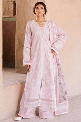 Woman wearing a light pink embroidered traditional outfit against a beige wall.