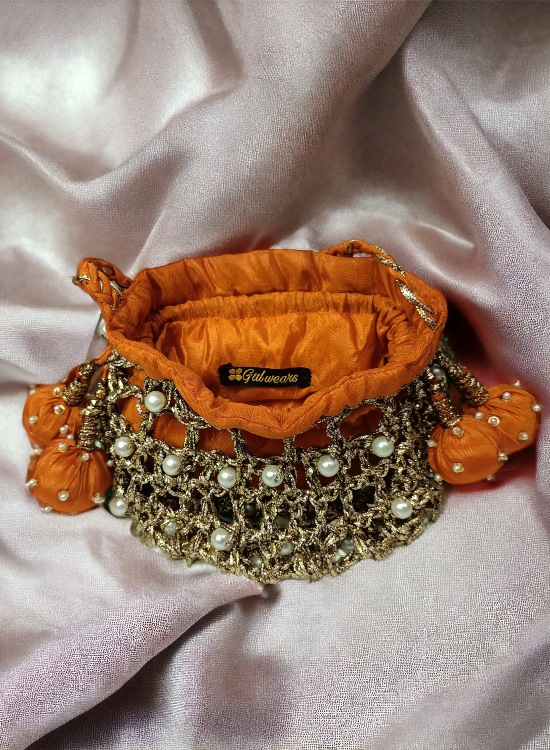 A bright orange potli bag with intricate copper gotta work, displayed on a shiny cloth.