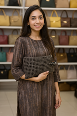 Woman holding a woven clutch in front of a display of handbags.