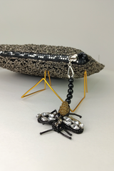 A black and silver fabric clutch bag with a floral pattern, displayed on a stand.