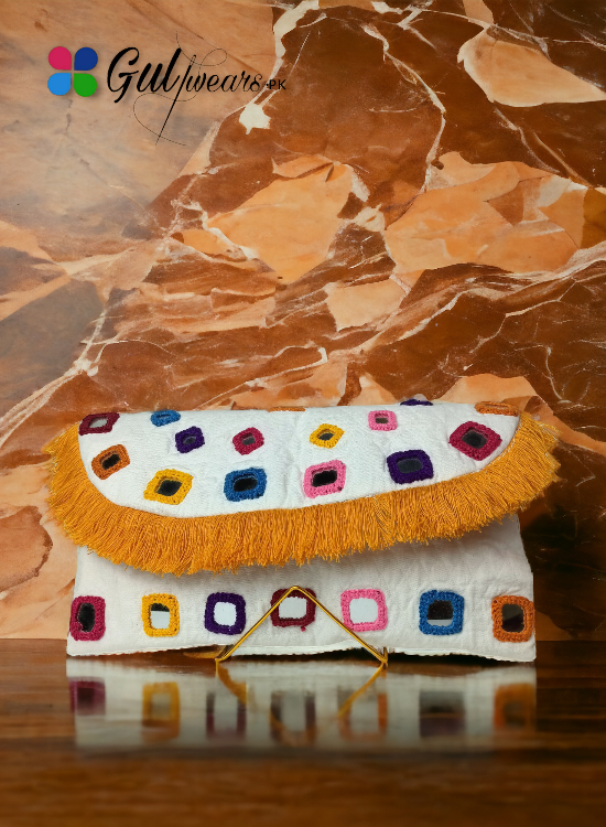 A white multicolor mirror worked clutch bag with a vibrant and colorful design, placed on a marble surface.